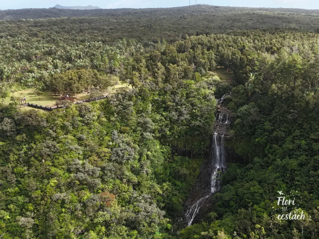 Letecký pohled z dronu na stupňovitý vodopád Alexandra Falls na Mauriciu padající skrze hustou zelenou džungli s dřevěnou vyhlídkovou platformou vlevo.