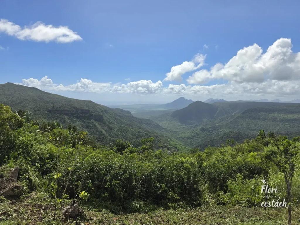 ýhled z vyhlídky Gorges Viewpoint do hlubokého zeleného kaňonu národního parku Black River Gorges na Mauriciu pod modrou oblohou s bílými mraky.
